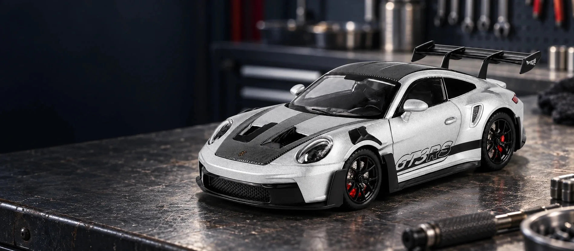 Silver Porsche 911 GT3 RS scale model on a dark garage workbench